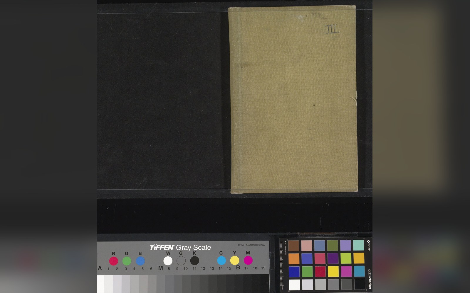 Worn tan cloth-bound sketchbook cover photographed beside a color and gray scale calibration chart