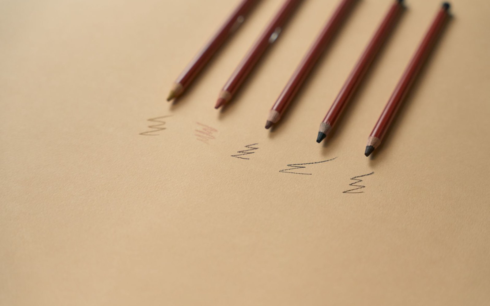Five colored pencils with squiggly test marks on tan toned paper