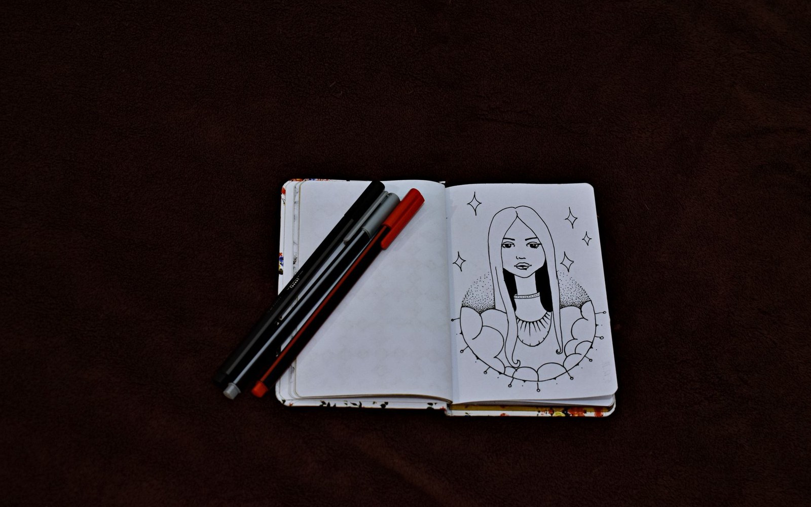 Open sketchbook shows a pen-and-ink portrait of a woman surrounded by stars and clouds